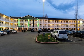 Un motel à plusieurs étages, doté d’une réception centrale, de nombreux balcons et d’un parking où sont stationnés plusieurs véhicules.