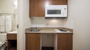 Una kitchenette pequeña con microondas, lavamanos y encimera.