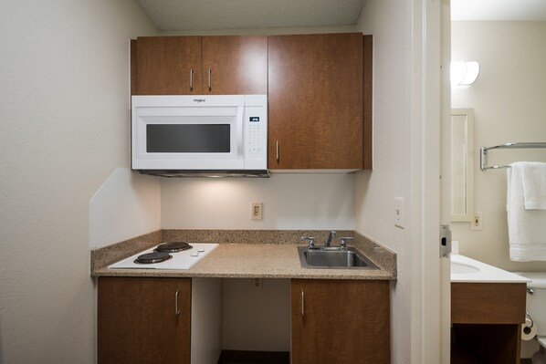 Una cocina compacta con microondas, pileta y armarios de madera.