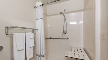 A shower area with a glass door, a handheld showerhead, a towel rack with folded towels, and a safety bar.