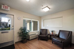 Zona de recepción con letrero de salida, un reloj, una ventana, una planta en maceta, dos sillones de cuero y una pequeña mesa.