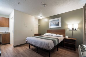 A hotel room with a bed, bedside tables, a nightstand, a wall-mounted lamp, a picture, and a radiator.