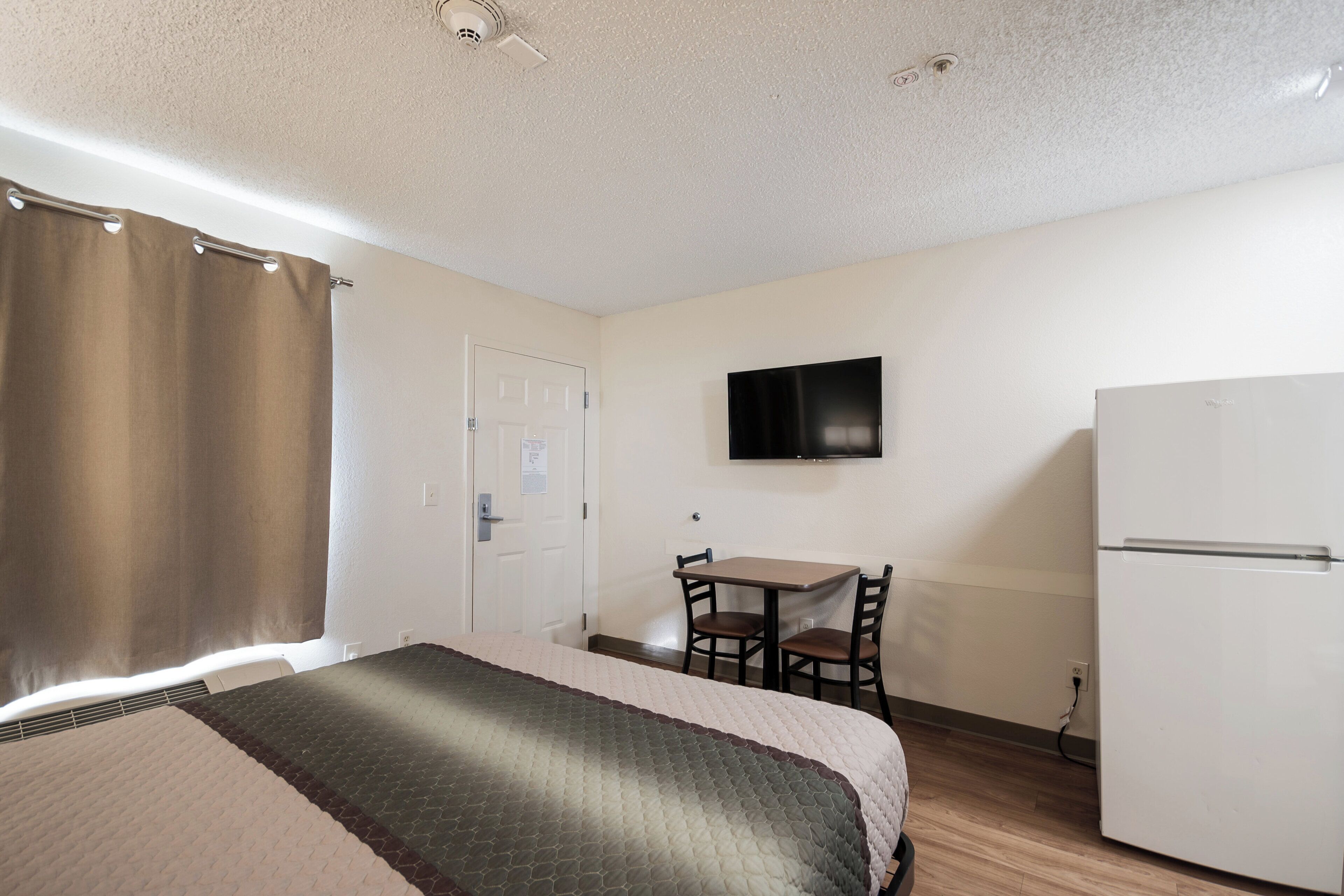 Una habitación de hotel con cama, escritorio con dos sillas, televisión y refrigerador.