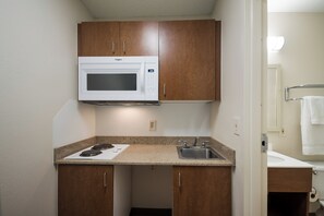 A compact kitchenette with a microwave, stove, and sink. - HomeTowne Studios By Red Roof Seattle - Kent/ Des Moines (Kent)