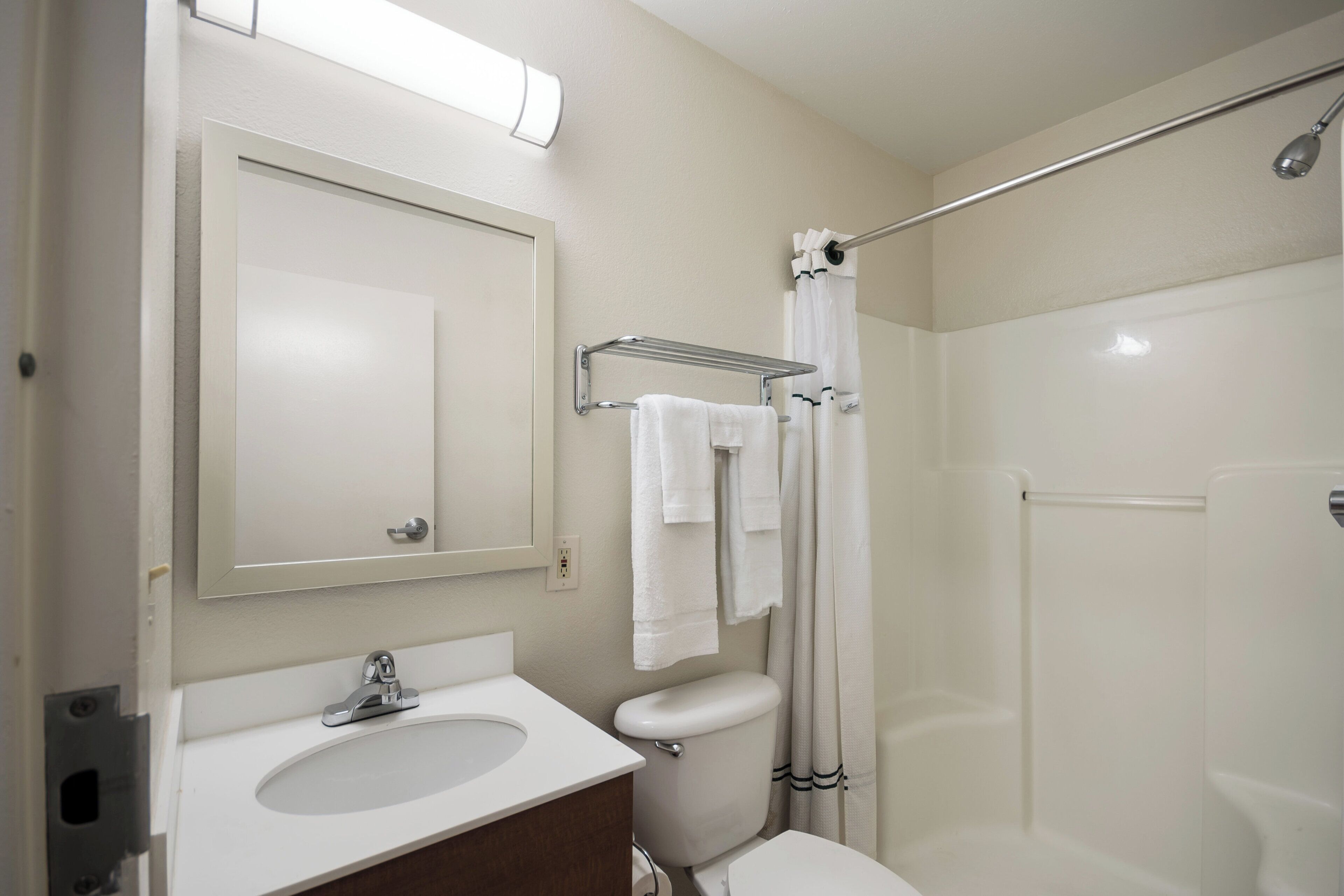 Un baño con lavamanos, espejo, toallero, inodoro y cortina de ducha.