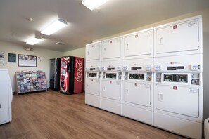 A laundry facility with multiple washing machines, a Coca-Cola vending machine, and a map display. - HomeTowne Studios By Red Roof Seattle - Kent/ Des Moines (Kent)
