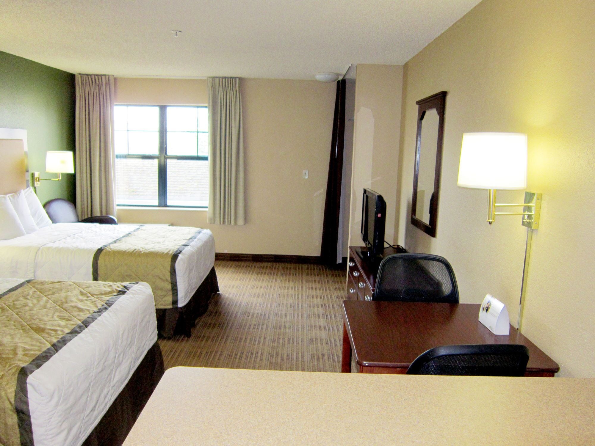 A hotel room with two beds, a desk with a chair, a television, and a lamp.