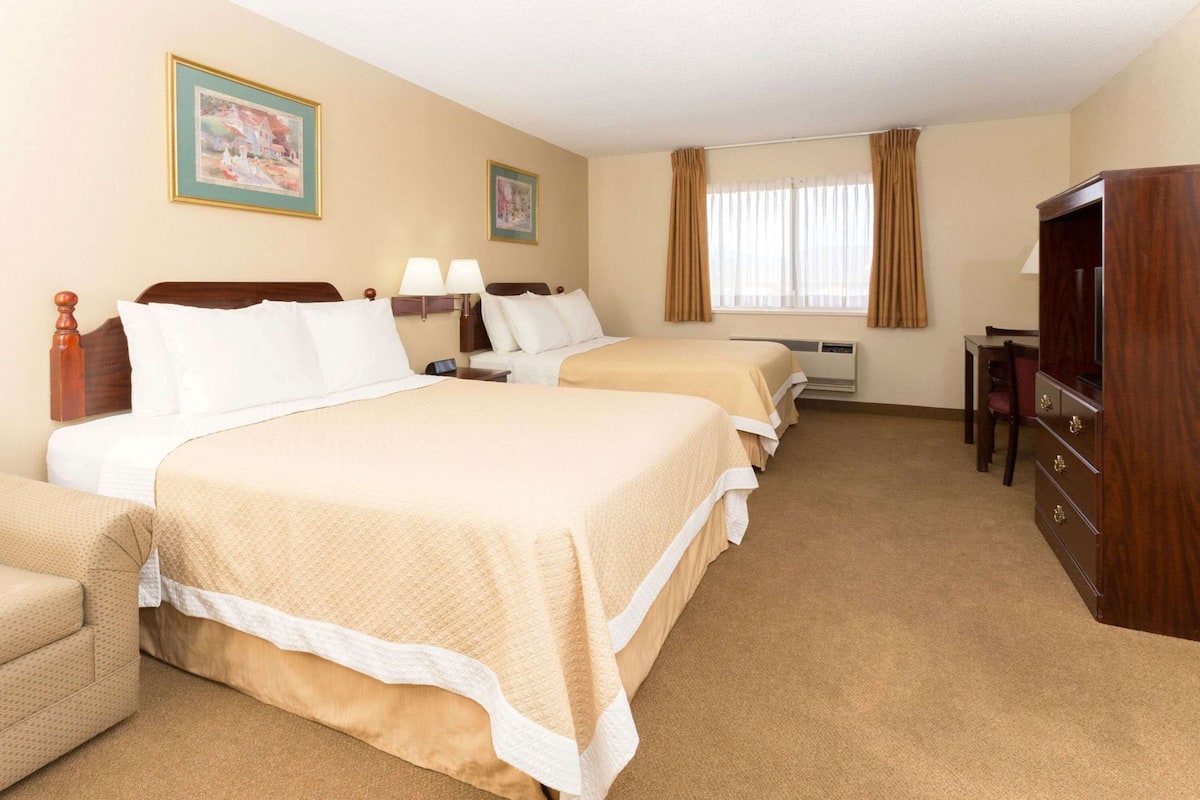 A hotel room with three beds, a TV, a desk, and two lamps.