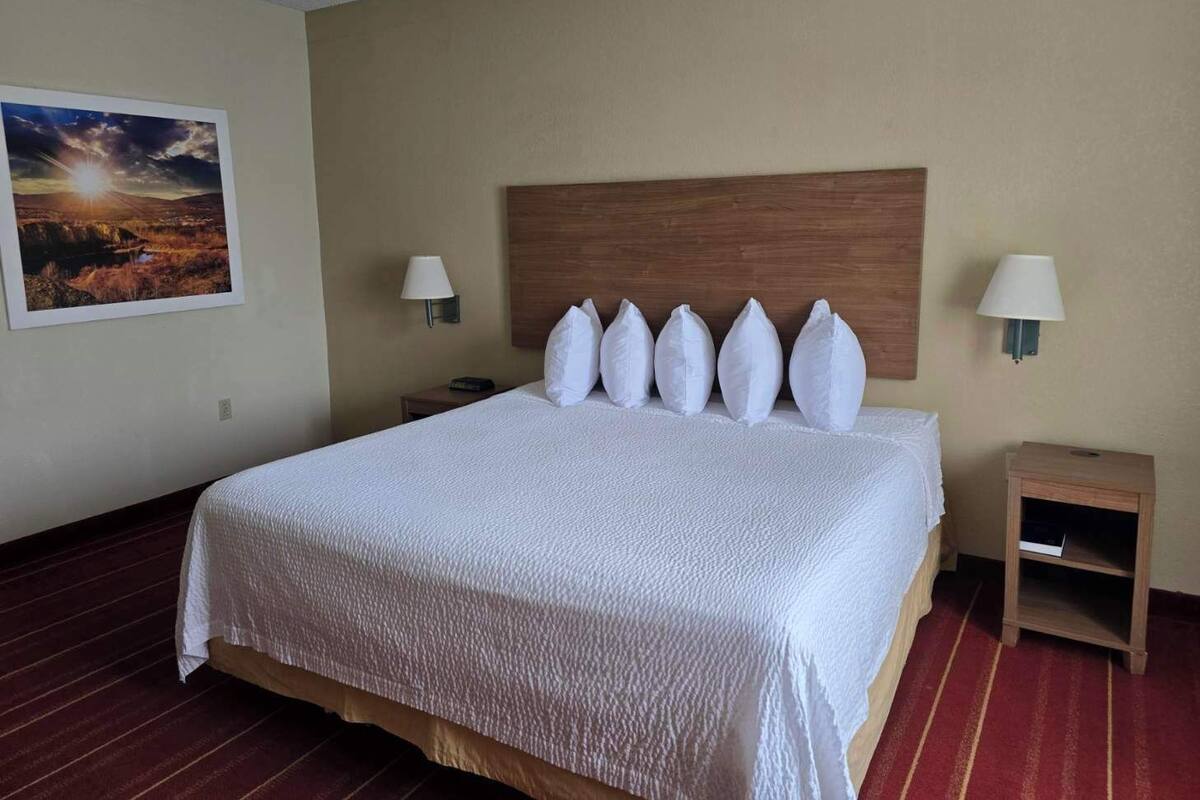 A hotel room with a large bed, a wooden headboard, two bedside tables with lamps, and a framed picture on the wall.