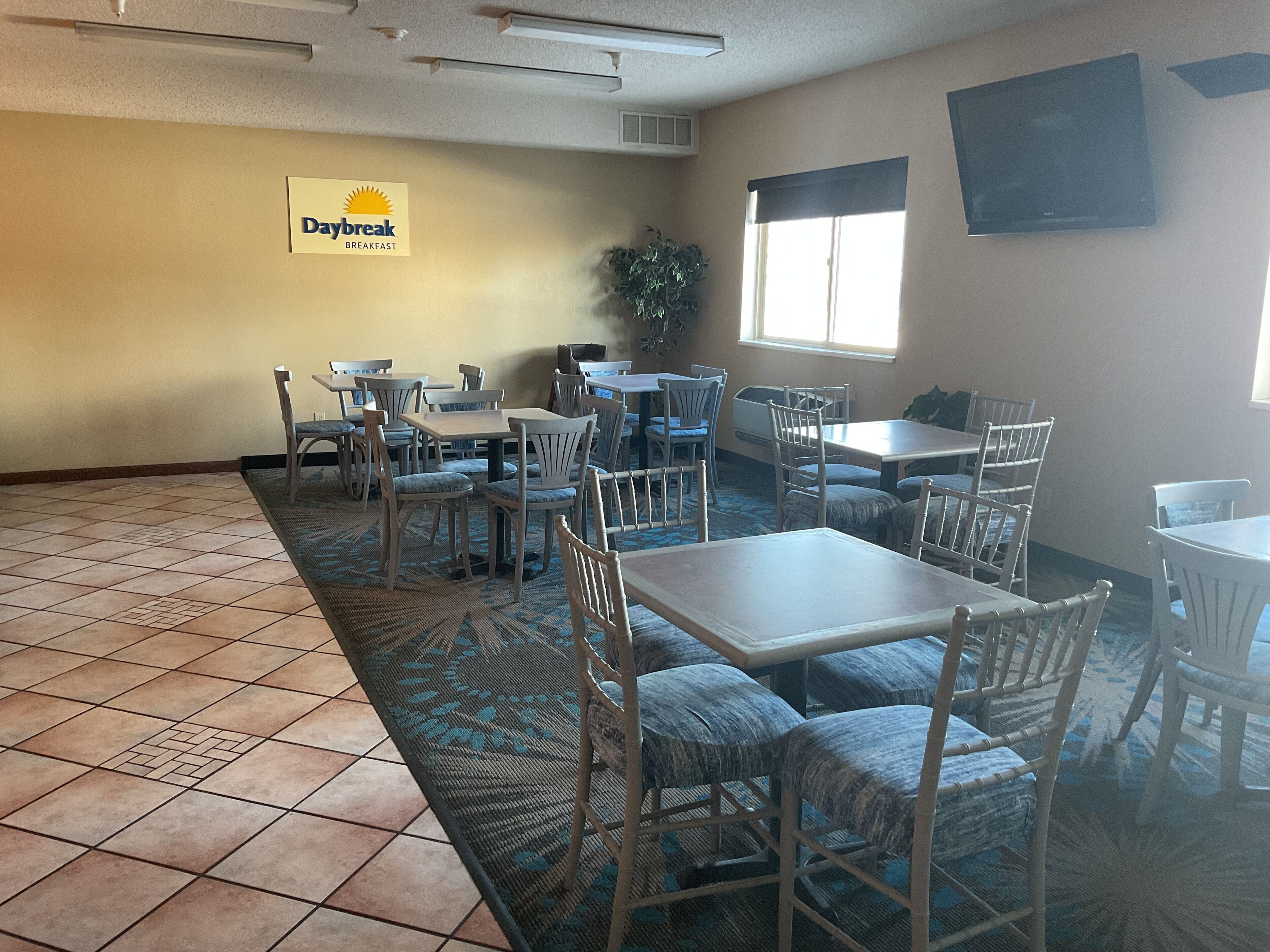 A dining area with multiple tables and chairs, a sign for 'Daybreak Breakfast', and a large window providing natural light.