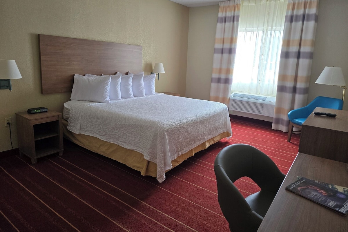 A hotel room with a bed, bedside tables, a desk, a chair, and a window with curtains.
