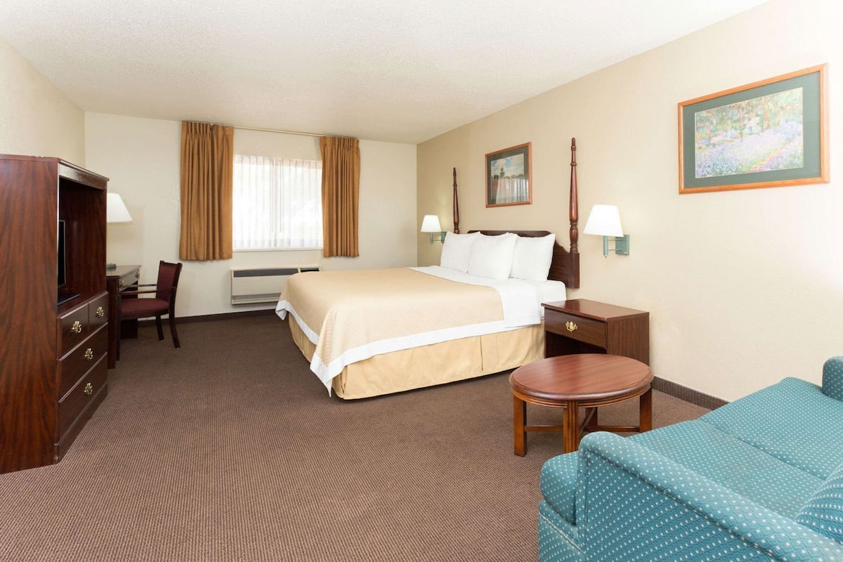 A hotel room with a bed, desk, chair, and a small table.