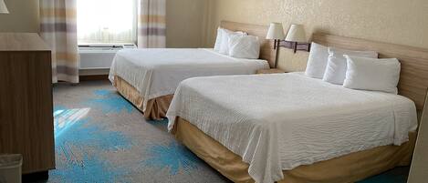 A hotel room with two beds, a desk, and a window with curtains.