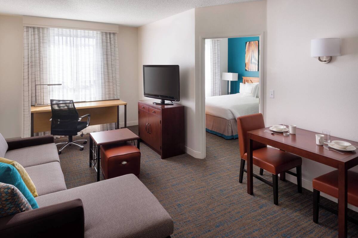 Een hotelkamer met een bank, een bureau met een televisie, een eettafel met stoelen en een bed op de achtergrond.