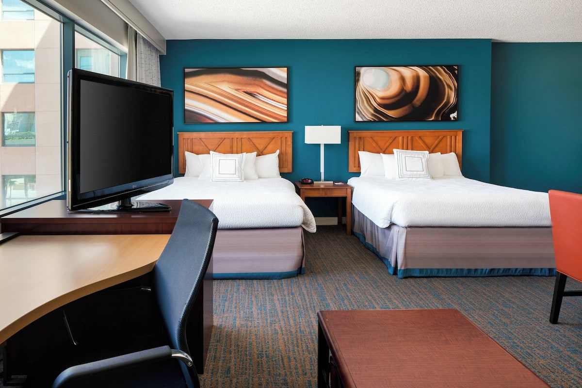 Een hotelkamer met twee bedden, een bureau, een stoel, een televisie en kunst aan de muren.