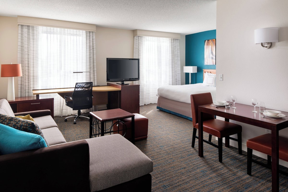 Een hotelkamer met een bed, een bureau met televisie, een eettafel met stoelen en een bank.