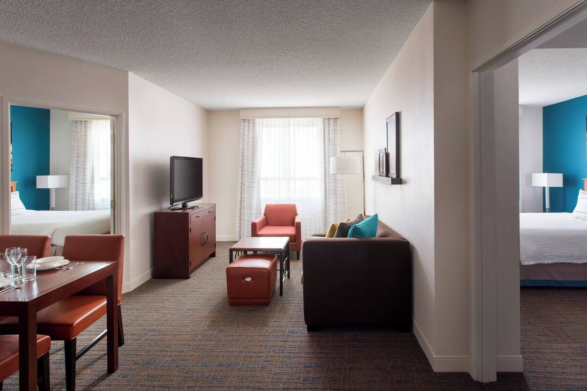Een hotelkamer met een bed, een bureau met stoel, een bank, een televisie en een raam met gordijnen.