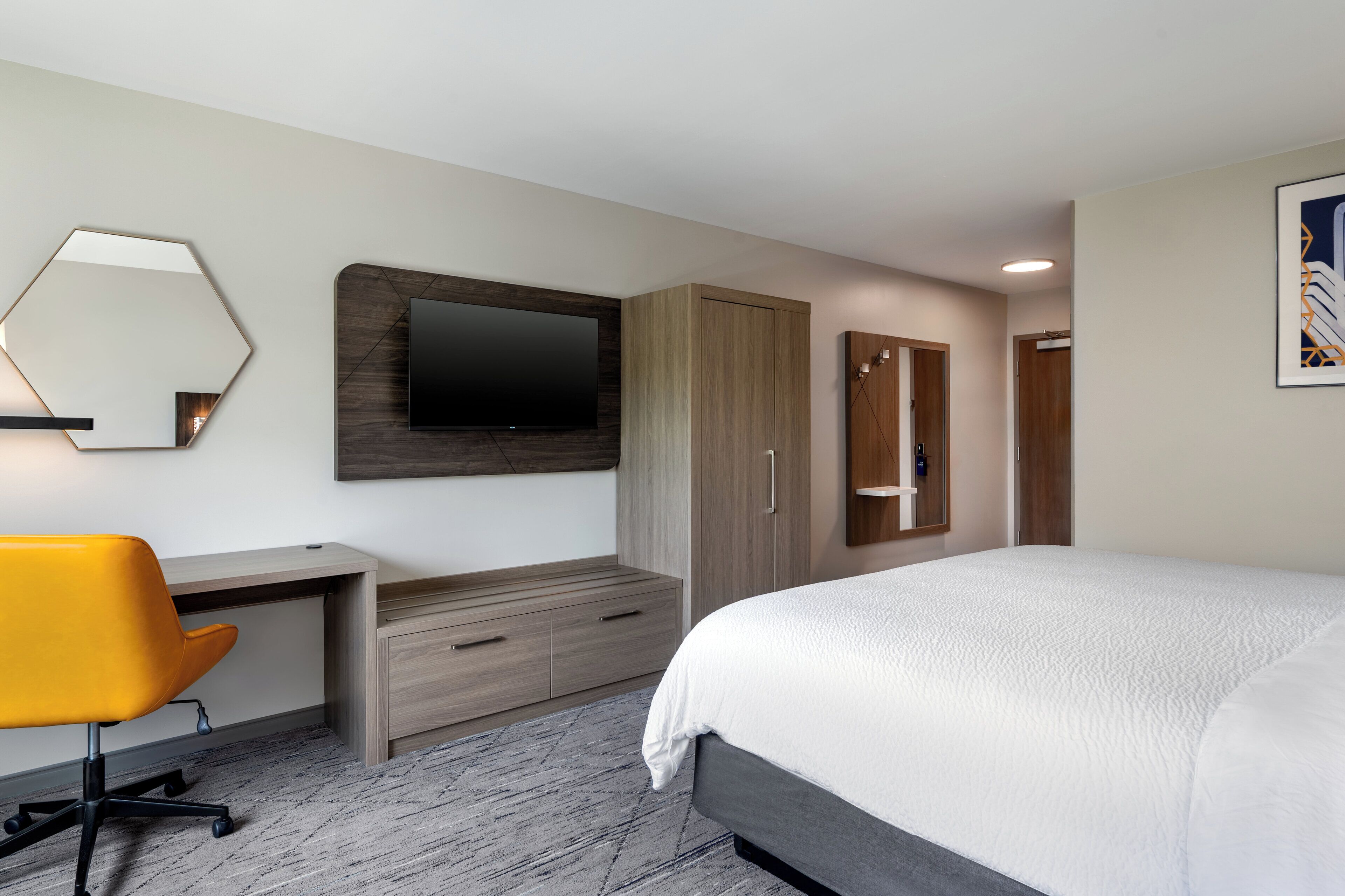 A modern hotel room with a bed, a desk with a chair, a TV, and a wardrobe.