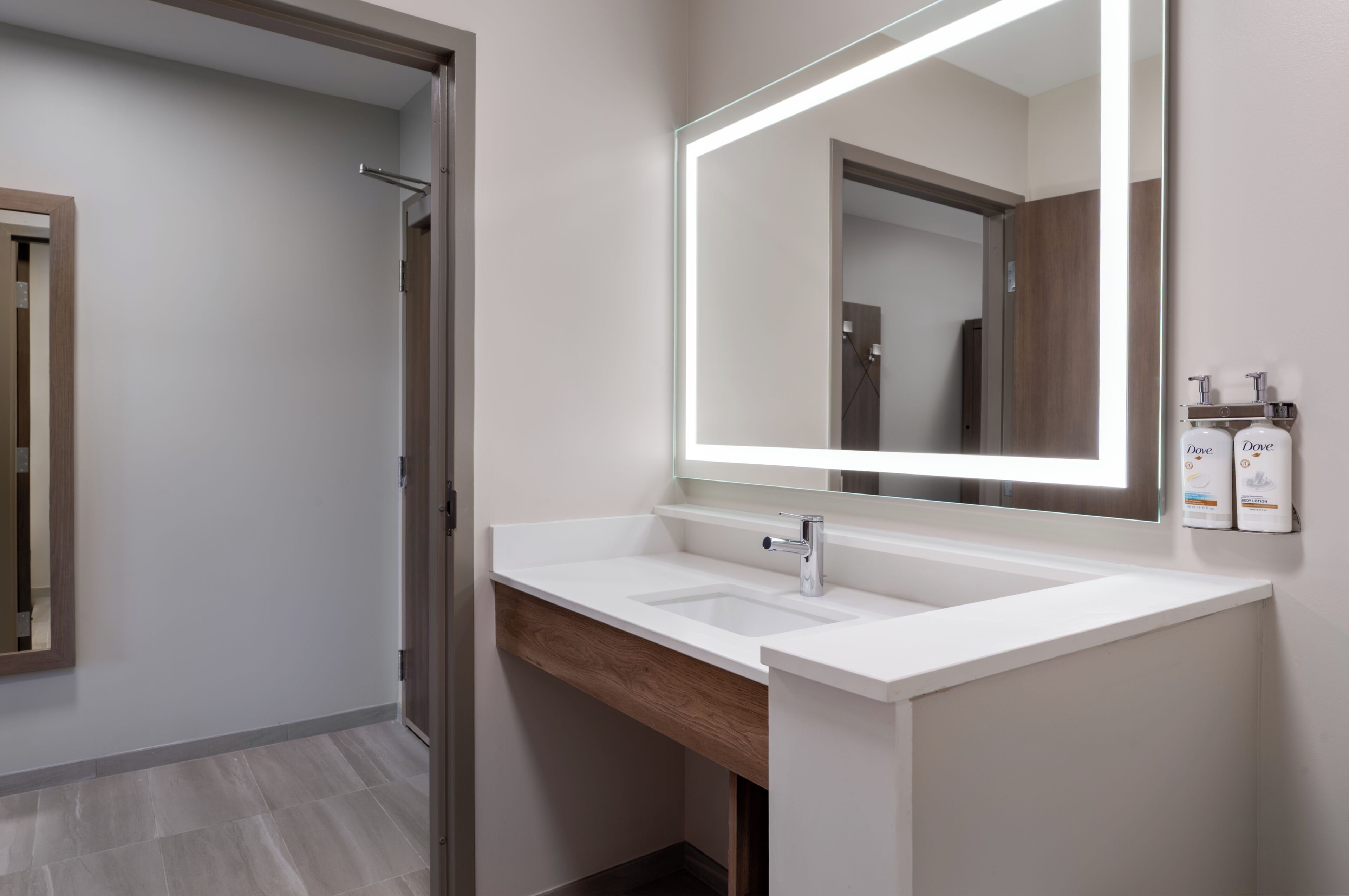 A modern bathroom with a white sink, a large mirror, and two toiletries on the wall.