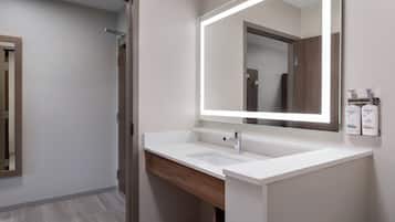 A modern bathroom with a white sink, a large mirror, and two toiletries on the wall.