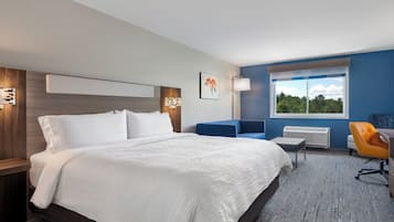 Quarto de hotel moderno com uma cama grande, uma escrivaninha, uma cadeira e uma janela com vista para árvores.