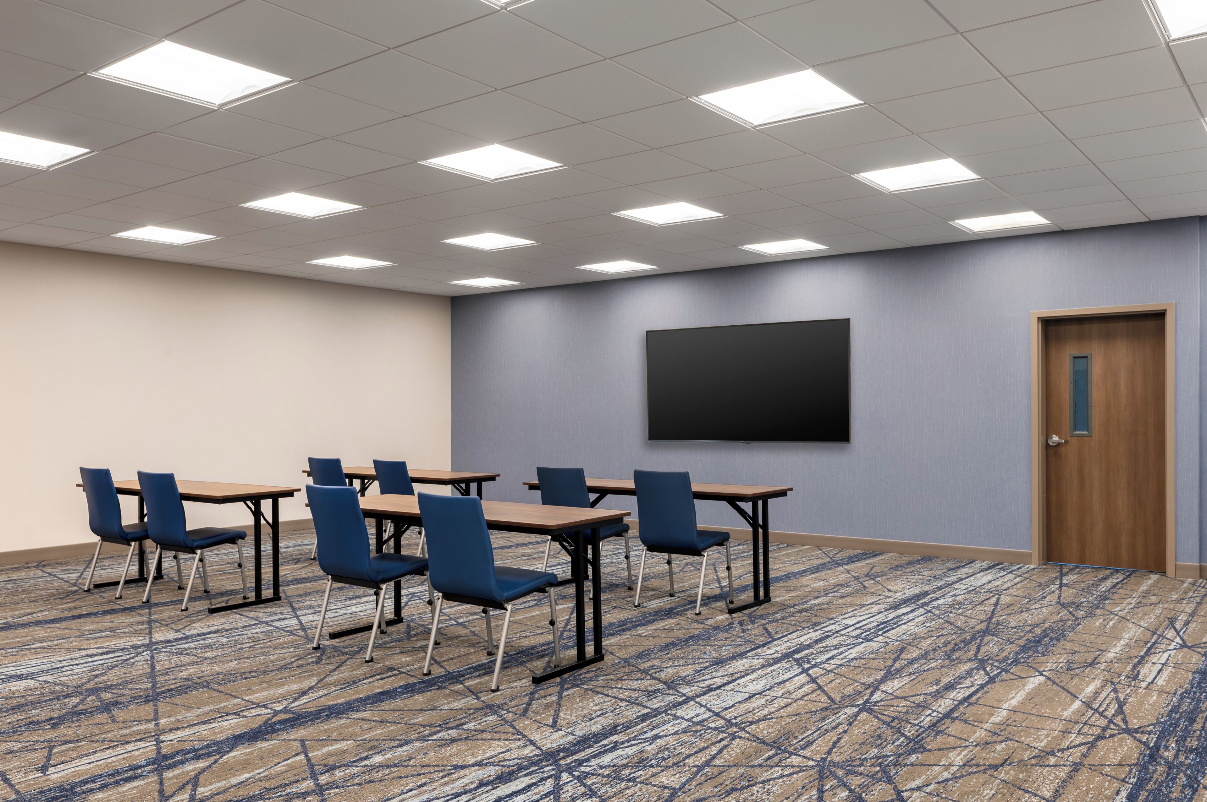 A conference room with a carpeted floor, tables, chairs, a projector screen, and a door.