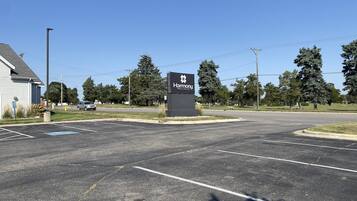 A Harmony Inn & Suites sign in a parking lot with a clear sky, trees, and a building in the background.