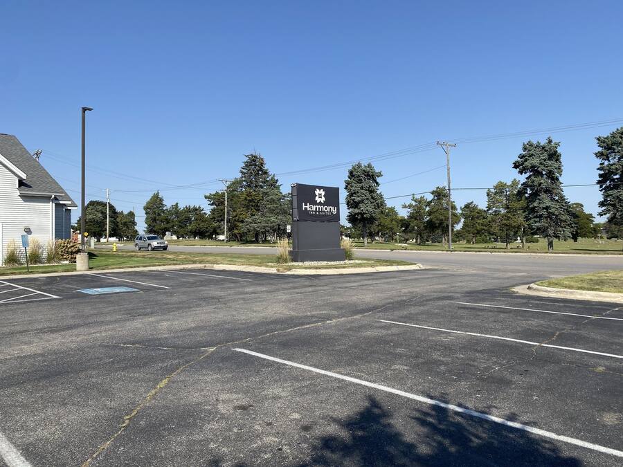 A Harmony Inn & Suites sign in a parking lot with a clear sky, trees, and a building in the background.