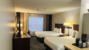 Ein Hotelzimmer mit zwei Betten, einem Schreibtisch, einem Stuhl, einer Lampe, einem Telefon und einem Fenster mit Vorhängen.