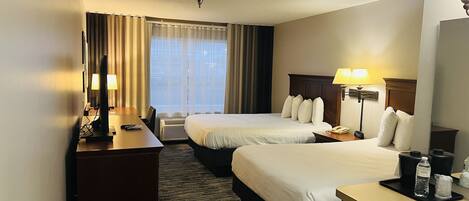 A hotel room with two beds, a desk, a chair, a lamp, a telephone, and a window with curtains.
