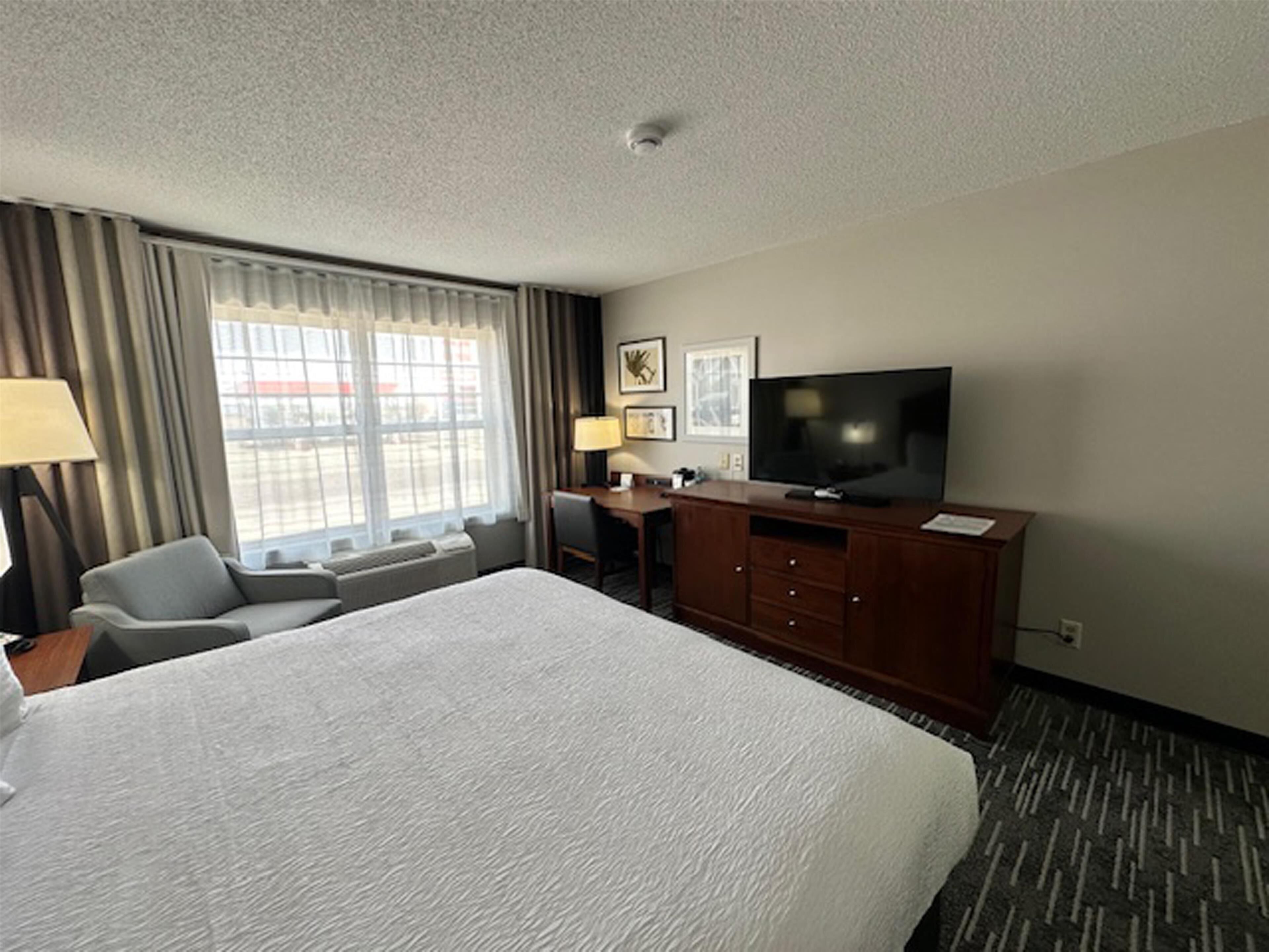 Habitación de hotel con una cama grande, un escritorio con silla, un televisor y una ventana con cortinas.
