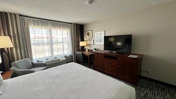 A hotel room with a large bed, a desk with a chair, a television, and a window with curtains.