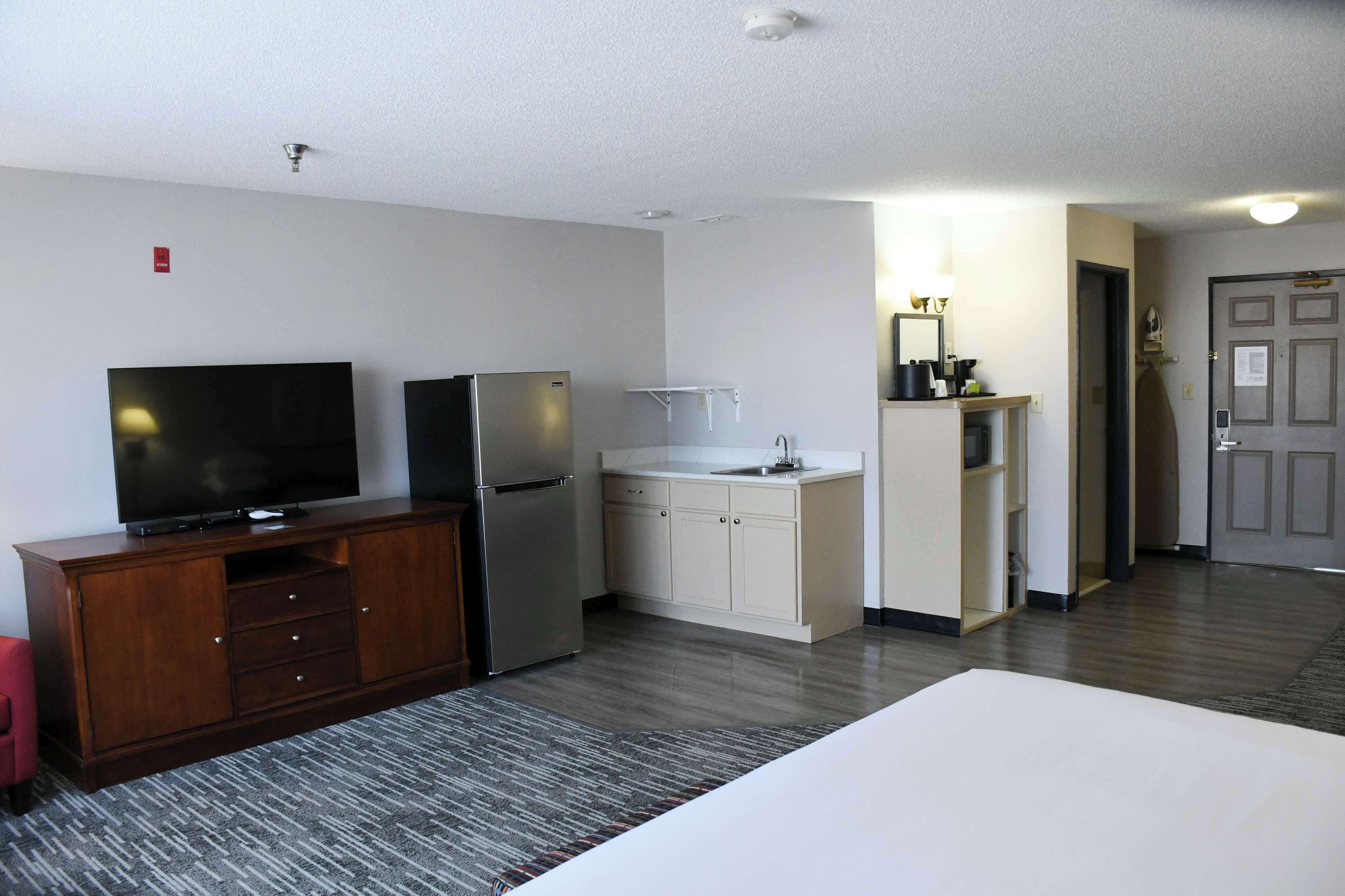 A hotel room with a TV, refrigerator, kitchenette, and a bed.
