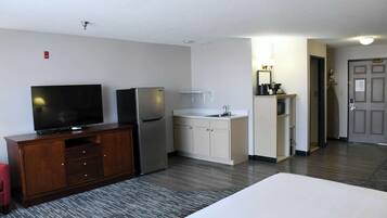A hotel room with a TV, refrigerator, kitchenette, and a bed.