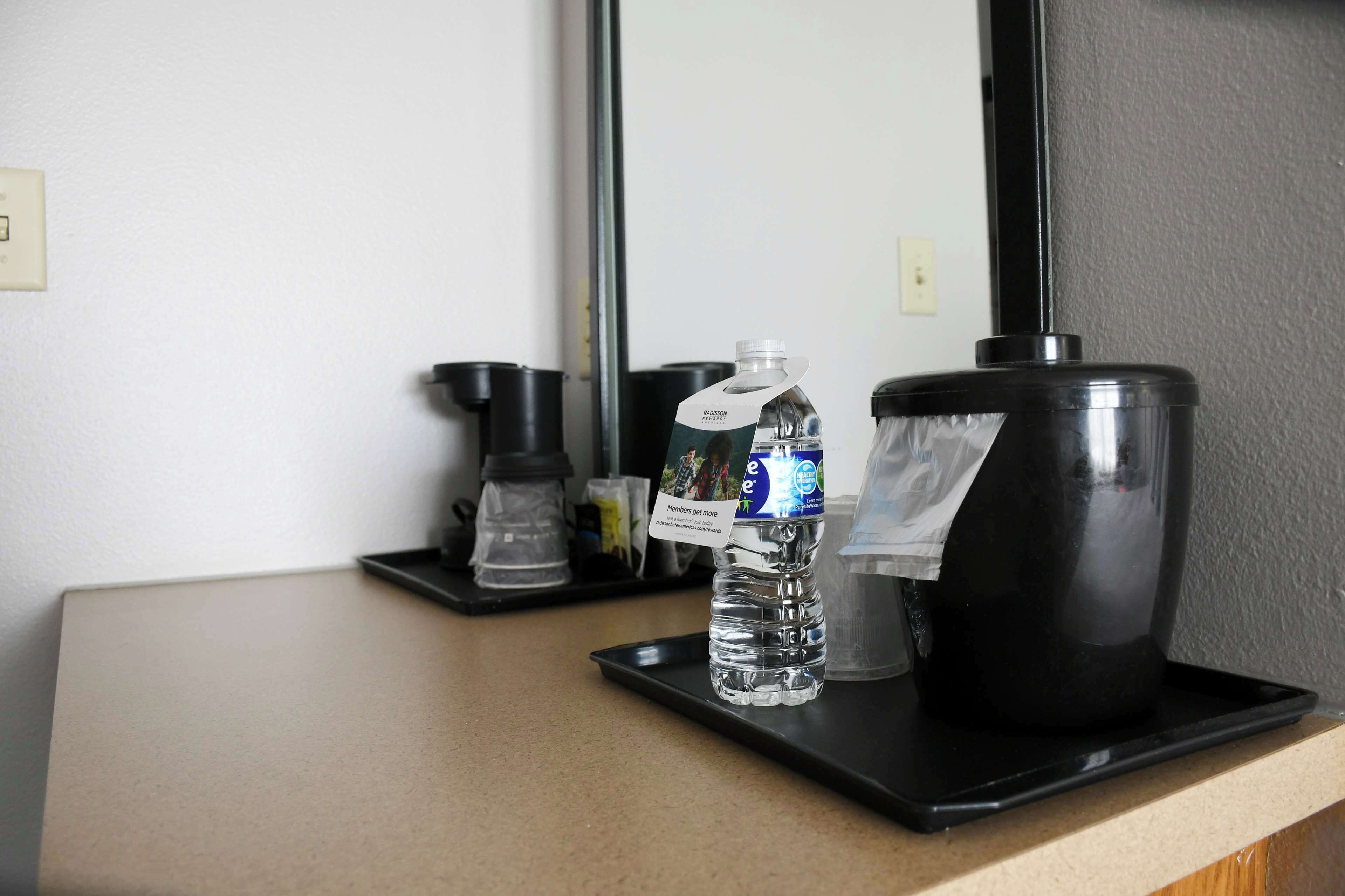 A hotel room counter with a water bottle, a coffee maker, and a trash bin.