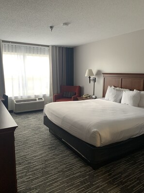 A hotel room with a large bed, a desk, a chair, a lamp, and a window with curtains.