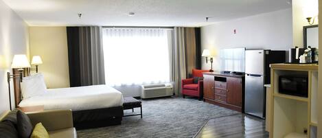 Habitación de hotel con cama, escritorio, silla, televisor y minibar.
