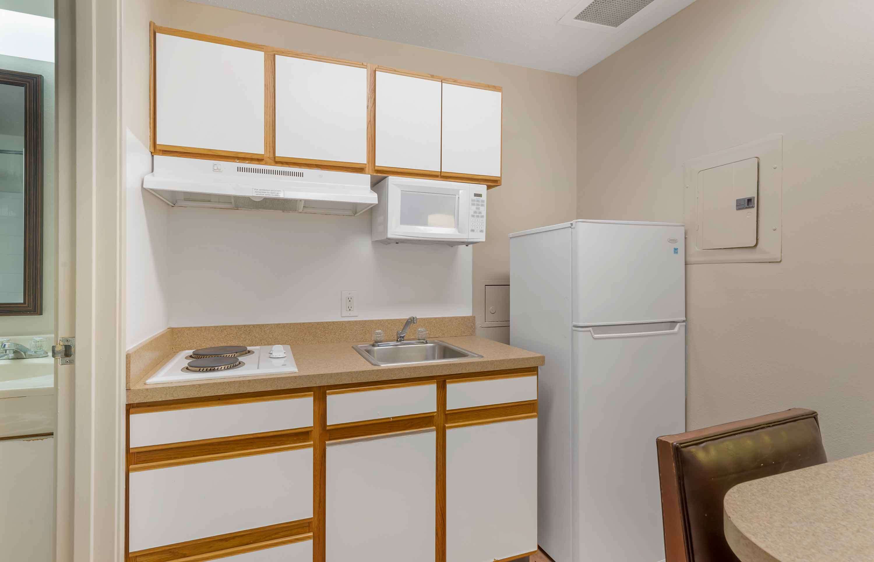 A compact kitchen with white cabinets, a microwave, a refrigerator, and a sink.