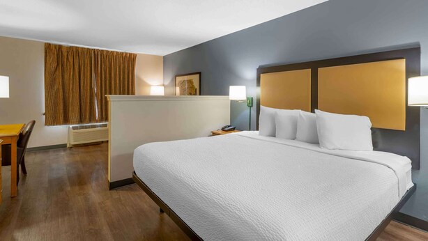 Habitación de hotel con una cama grande, un escritorio y una silla. Tiene una ventana con cortinas, una lámpara de pared y un cuadro en la pared.