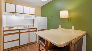 Una cocina compacta con comedor, armarios blancos, un refrigerador y una lámpara fijada a la pared.