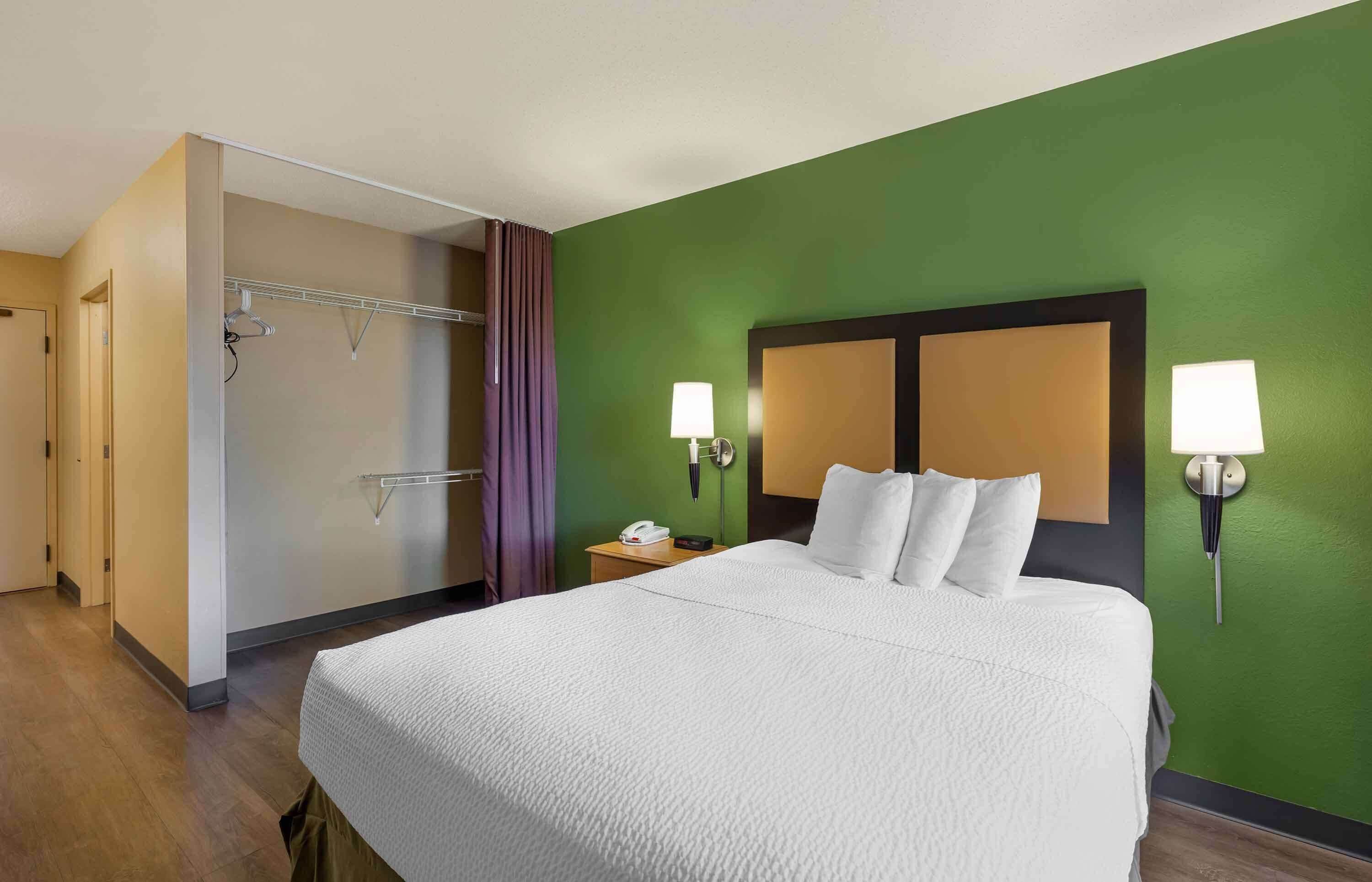 Habitación de hotel con una cama grande, dos lámparas de noche, una mesita de noche, un teléfono y una pared de acento verde.