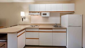 Una cocina compacta con armarios blancos, un microondas, una estufa, un lavabo y un refrigerador.