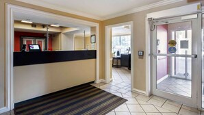 Un hall de hotel con una recepción, un suelo a rayas y una entrada con puerta de cristal.