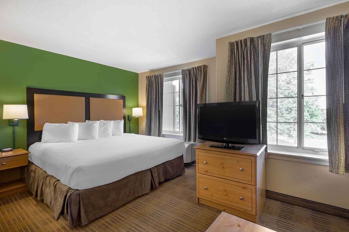 A hotel room with a large bed, a flat-screen TV, a dresser, and a window with curtains.