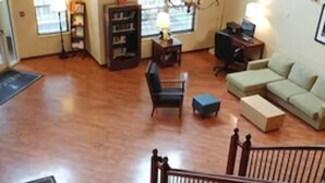 A spacious living area with a chandelier, a sofa, a chair, and a desk with a lamp. There is a staircase with a railing leading to an upper level.