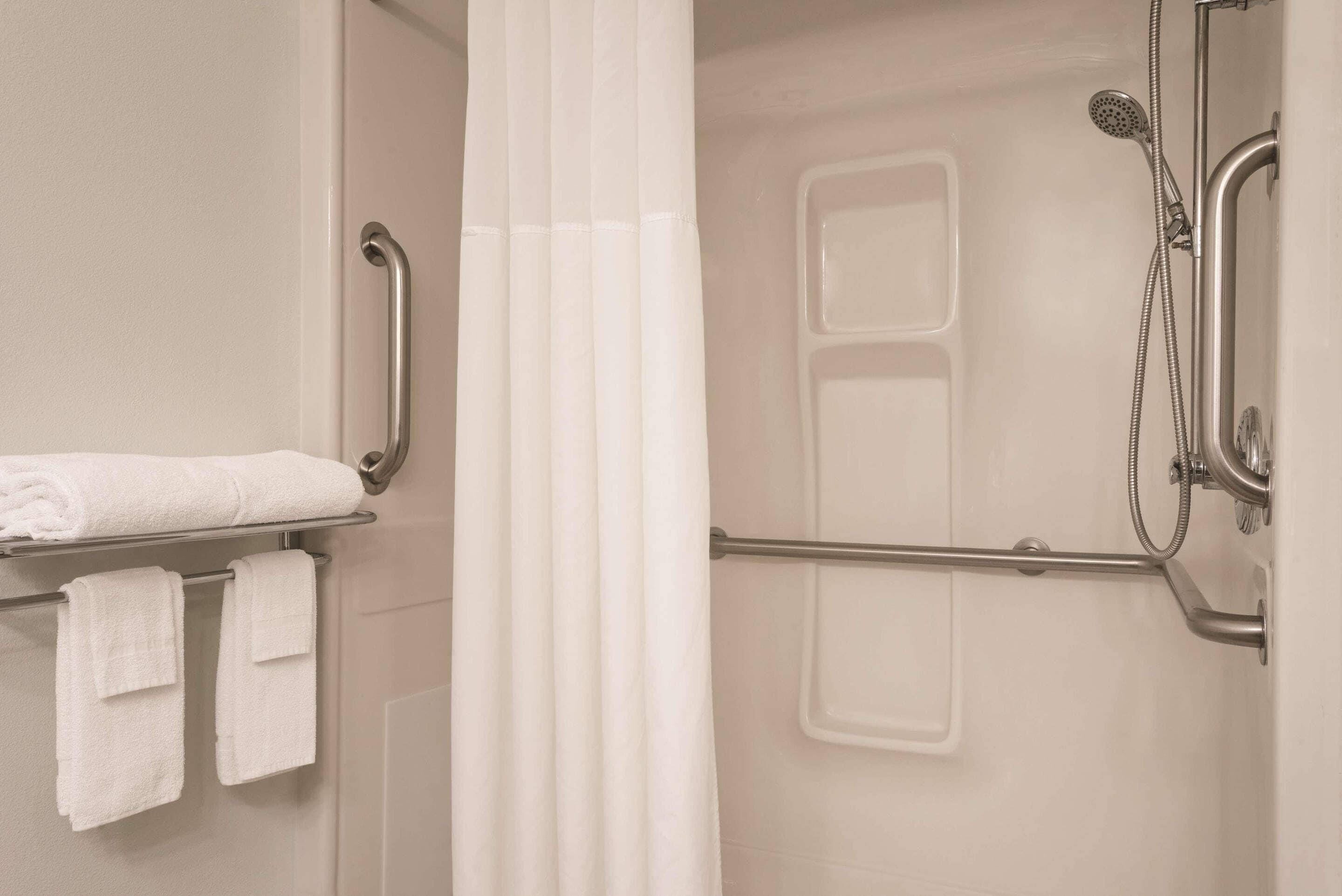 A shower area with a grab bar, a towel rack with towels, and a showerhead.