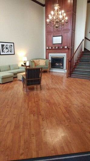 A spacious living room with hardwood flooring, a green sofa, a wooden chair, a fireplace, and a staircase.