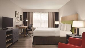 A hotel room with a bed, a desk, a TV, and a red chair.