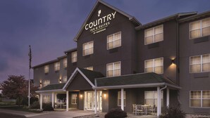 A Country Inn & Suites building with a modern design, featuring a prominent sign, multiple windows, and a covered outdoor seating area.