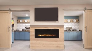A modern kitchen with a built-in fireplace, blue cabinets, and a flat-screen TV above the mantel.
